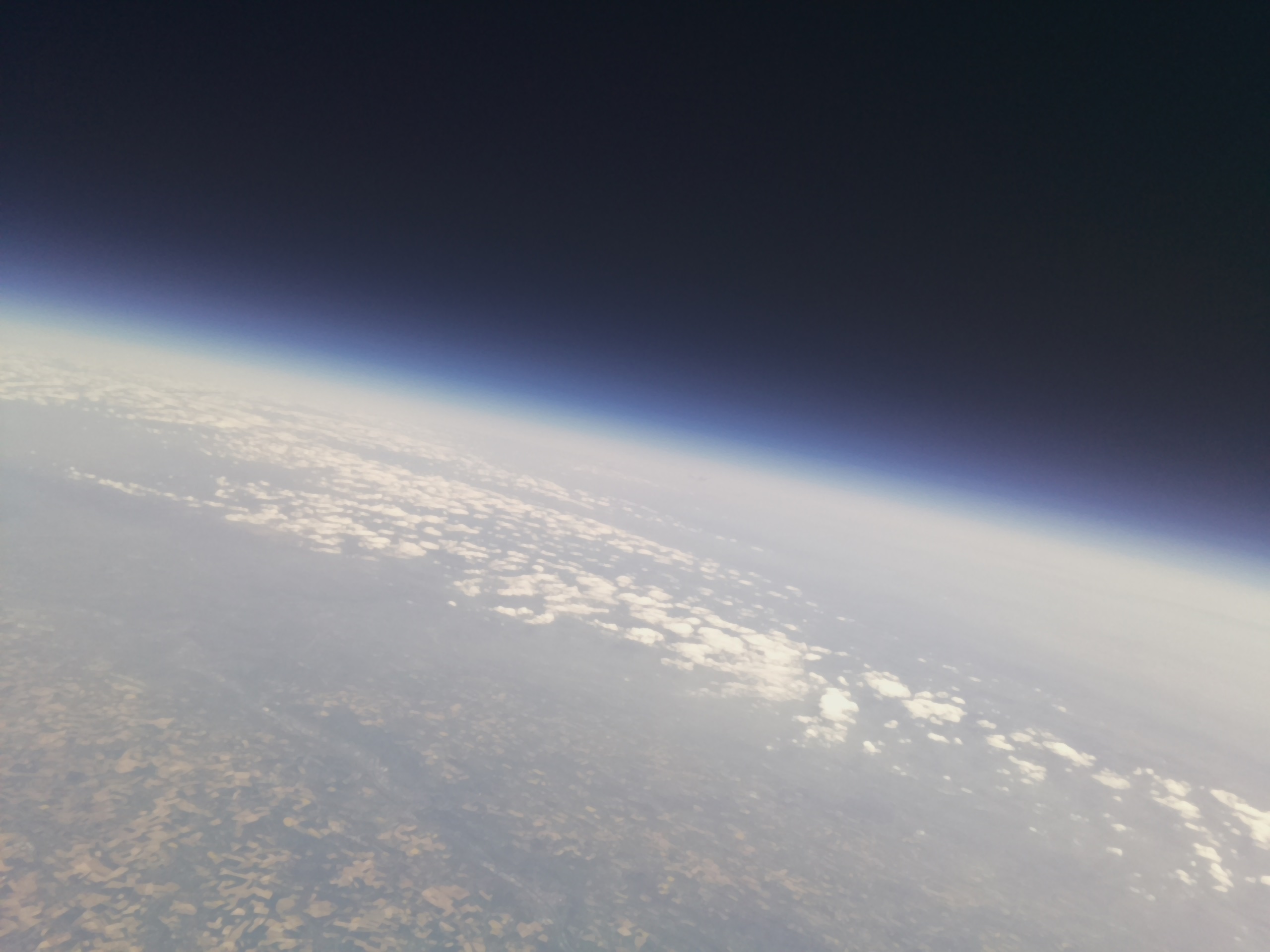 The Earth captured from the stratosphere on the Asgard XI mission, covered by clouds and fog, showing a bright blue transition from atmosphere to space.